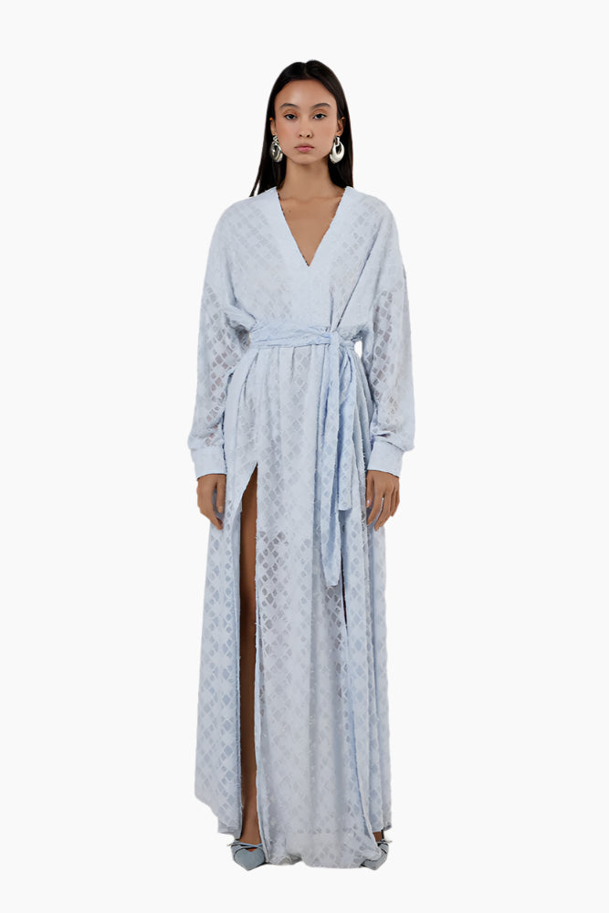 Woman wearing a light blue patterned dress with a slit. Flared floor-length dress with a V-neckline, balloon sleeves, two side slits, and a waist belt.