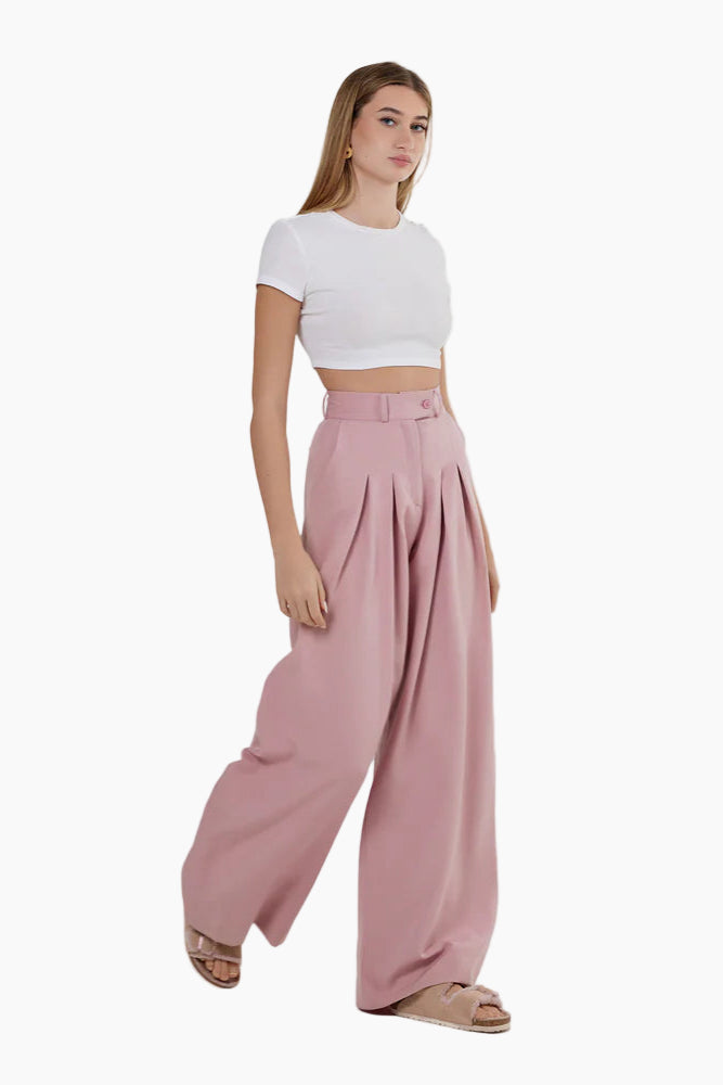 Woman wearing a white crop top and pink wide-leg pants on a white background