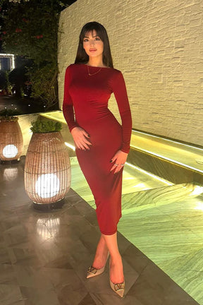 Woman in a red dress standing by a poolside at night.