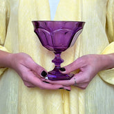 Purple glass goblet held by hands against a yellow fabric background