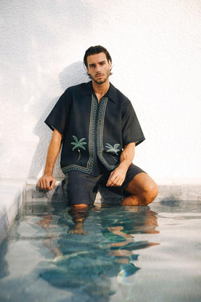 A man sitting in water wearing a black shirt with a geometric pattern.