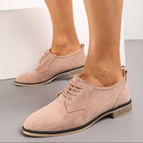 Beige suede shoes worn by a person on a neutral background