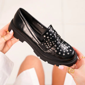Black leather loafer with silver studs held by a person against a light background