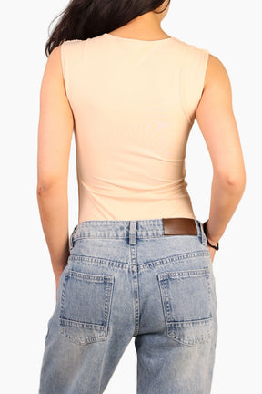 Person wearing a beige sleeveless top and blue jeans 
