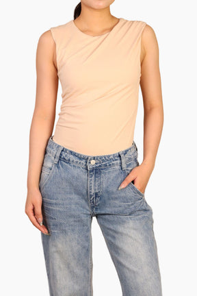 Person wearing a beige sleeveless top and blue jeans 