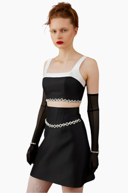 Model wearing a black and white outfit, crop top and skirt with chain with long gloves 