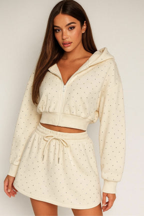 Woman wearing a cream polka dot hoodie and skirt set on a plain background