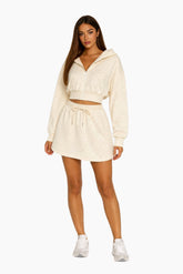 Woman wearing a cream-colored hoodie and skirt set on a white background
