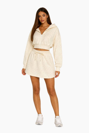 Woman wearing a cream-colored hoodie and skirt set on a white background