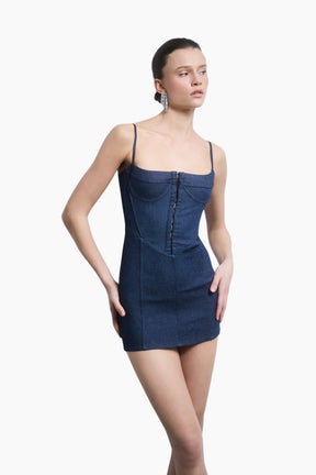 model wearing a classic denim mini with a structured silhouette and a corset-inspired bodice. The sculpting cut highlights the waist, while delicate straps and a front hook-and-eye closure balance strength with femininity.