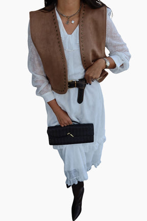 Person wearing a brown vest over a white dress with a black handbag 