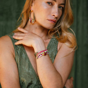 Woman wearing gold hoop earrings and a bracelet with a green background