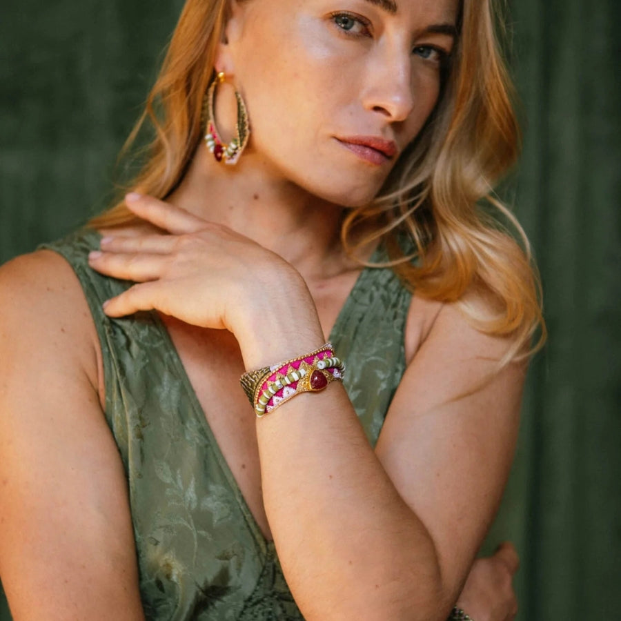 Woman wearing gold hoop earrings and a bracelet with a green background