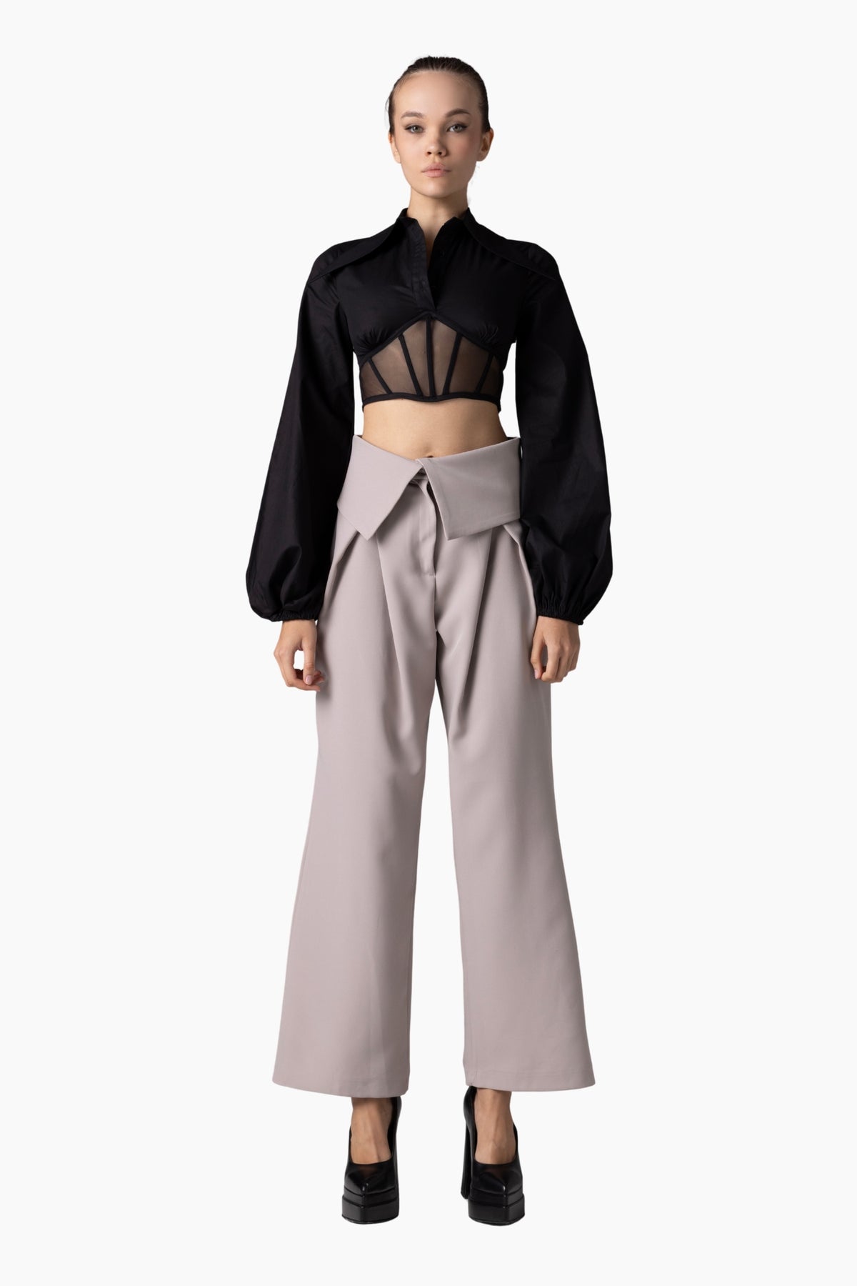 Woman wearing a black top with sheer design and light gray pants on a white background