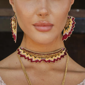 Close-up of a person wearing gold and red embroidered jewelry including earrings and a necklace.