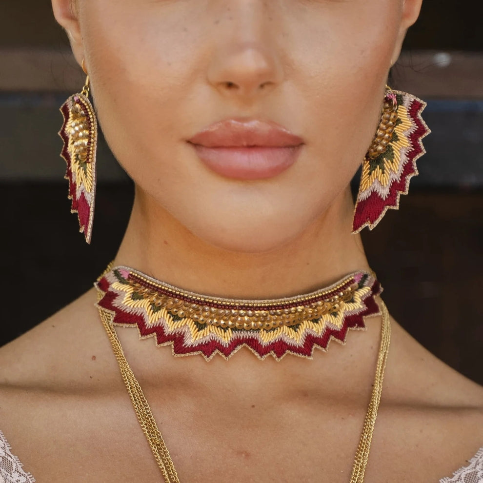 Close-up of a person wearing gold and red embroidered jewelry including earrings and a necklace.