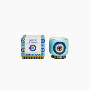 Decorative candle with blue and white design next to its packaging on a white background