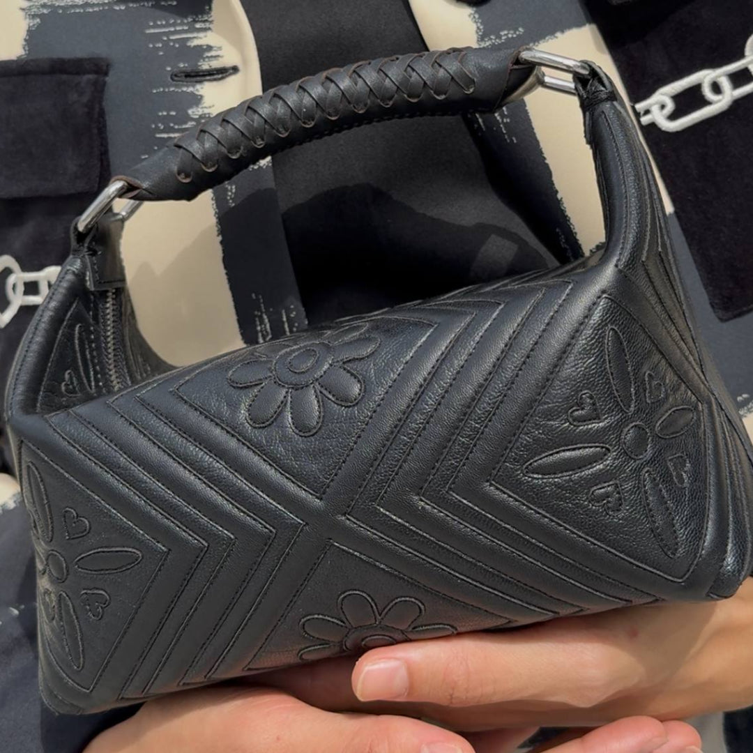 Black handbag with floral embossing held by a person against a blurred background