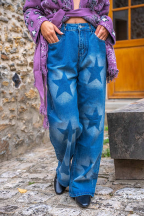 Person wearing blue jeans with star patterns and a purple scarf in an outdoor setting.