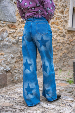 Person wearing blue jeans with star patterns standing against a stone wall.