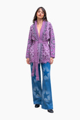 Woman wearing a purple patterned jacket and blue pants with star designs on a white background