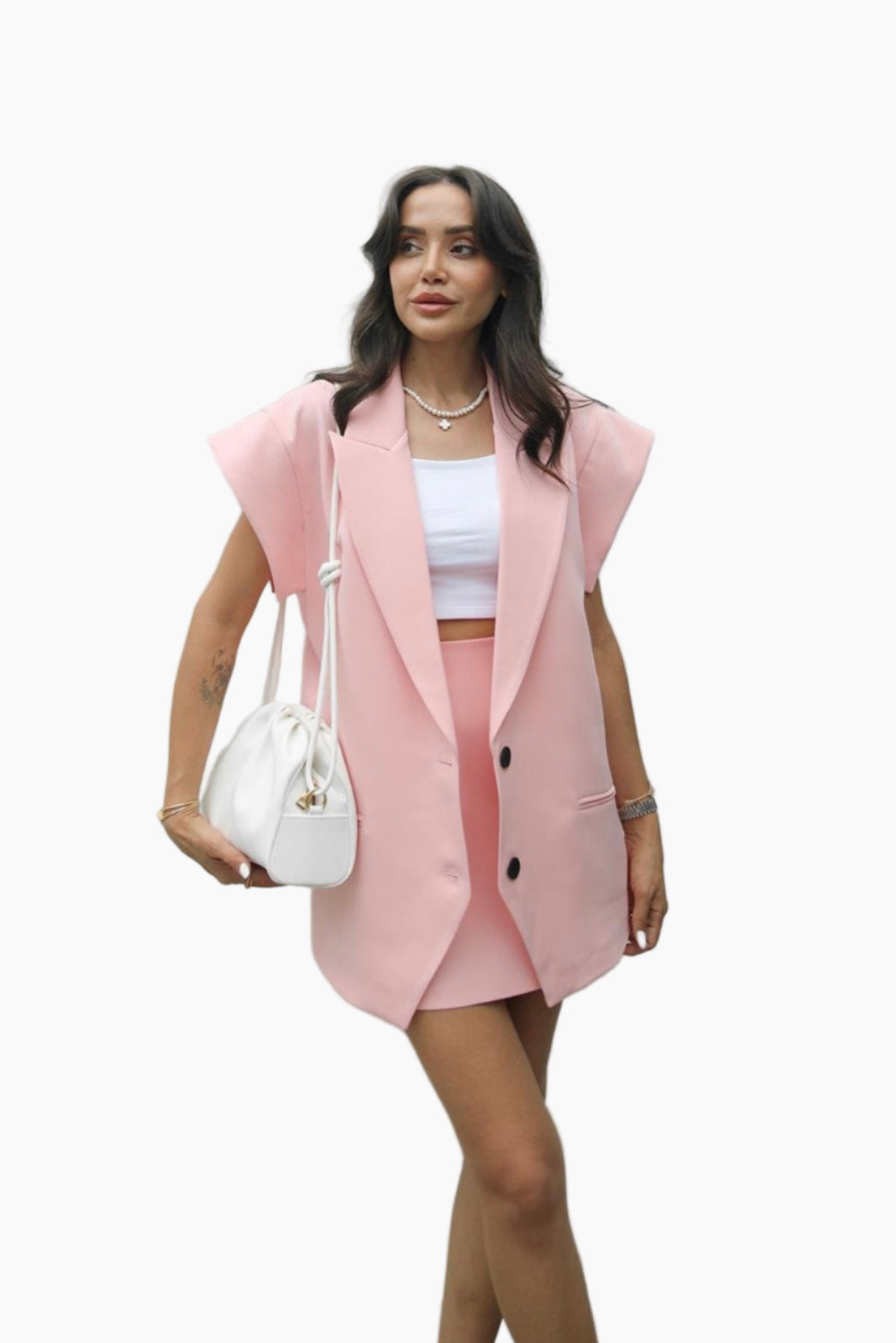 Woman wearing a pink blazer and skirt with a white top, holding a white handbag on a white background.