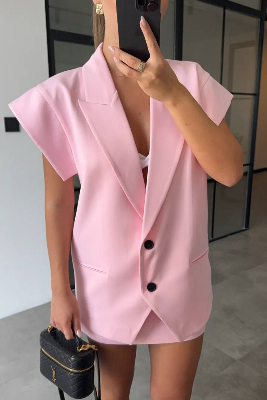 Person wearing a pink blazer dress holding a black handbag indoors.