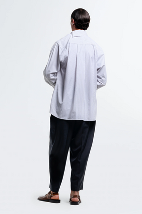 Person wearing a light gray striped shirt and dark pants on a white background