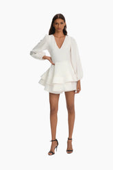 Woman wearing a white dress with long sleeves, soft linen fabric, invisible zipper fastening at the back.