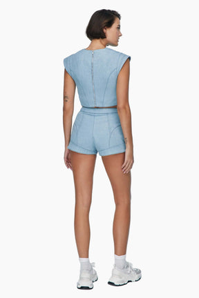 Woman wearing a light blue denim outfit. denim short Feature mid-rise belt. It is secured with a metallic button and a zipper fastening.

