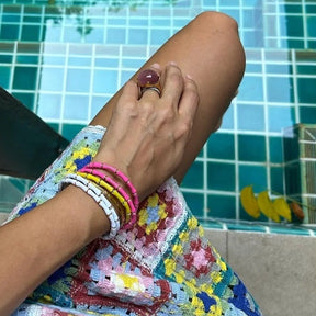 Close-up of a person's hand with colorful bracelets by a pool.
