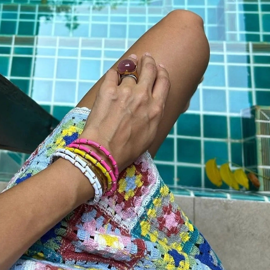 Close-up of a person's hand with colorful bracelets by a pool.