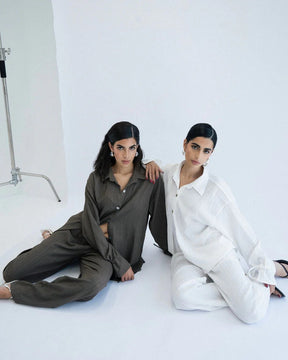 Two women sitting on a white floor, one in a green outfit and the other in a white outfit,