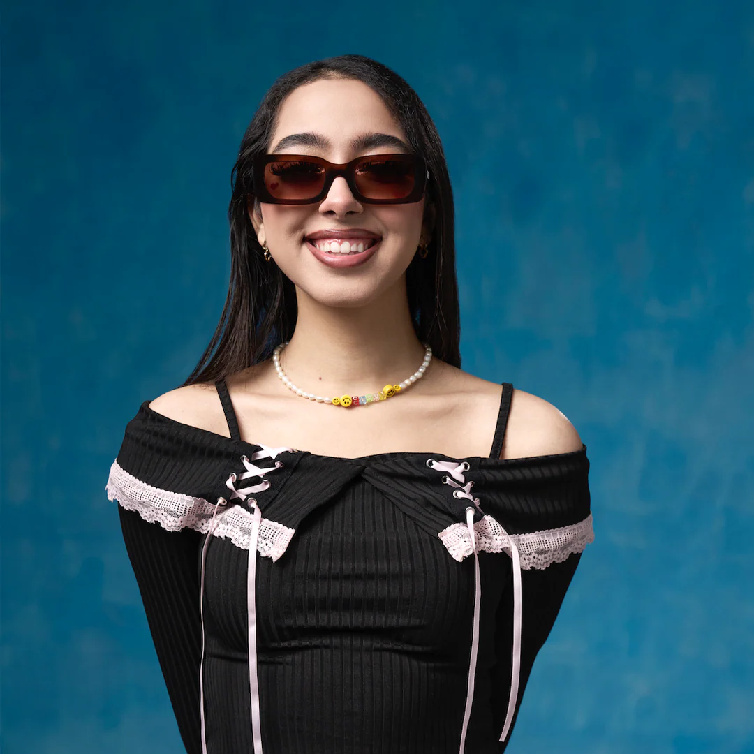 Woman wearing a black dress with lace details and sunglasses against a blue background