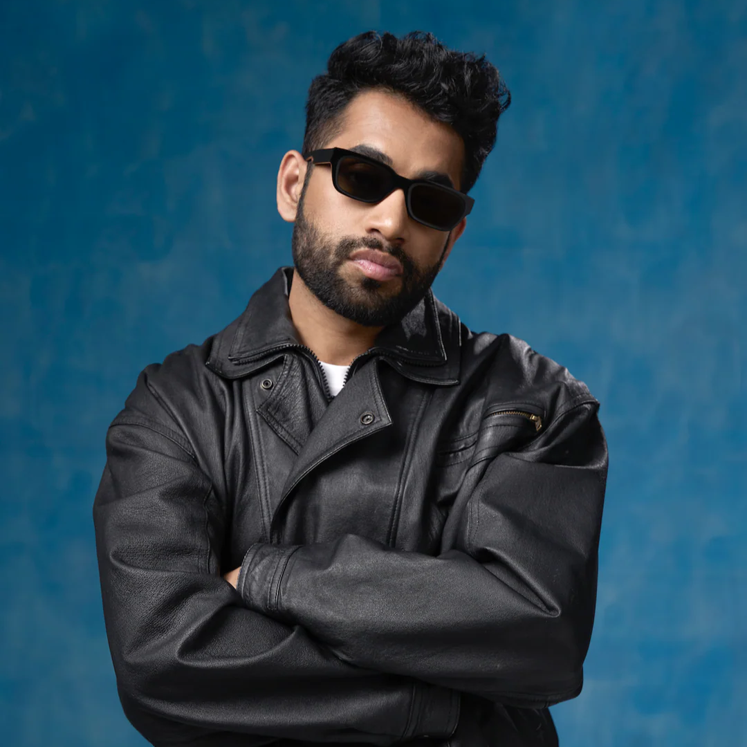 Man wearing a black leather jacket and sunglasses against a blue background