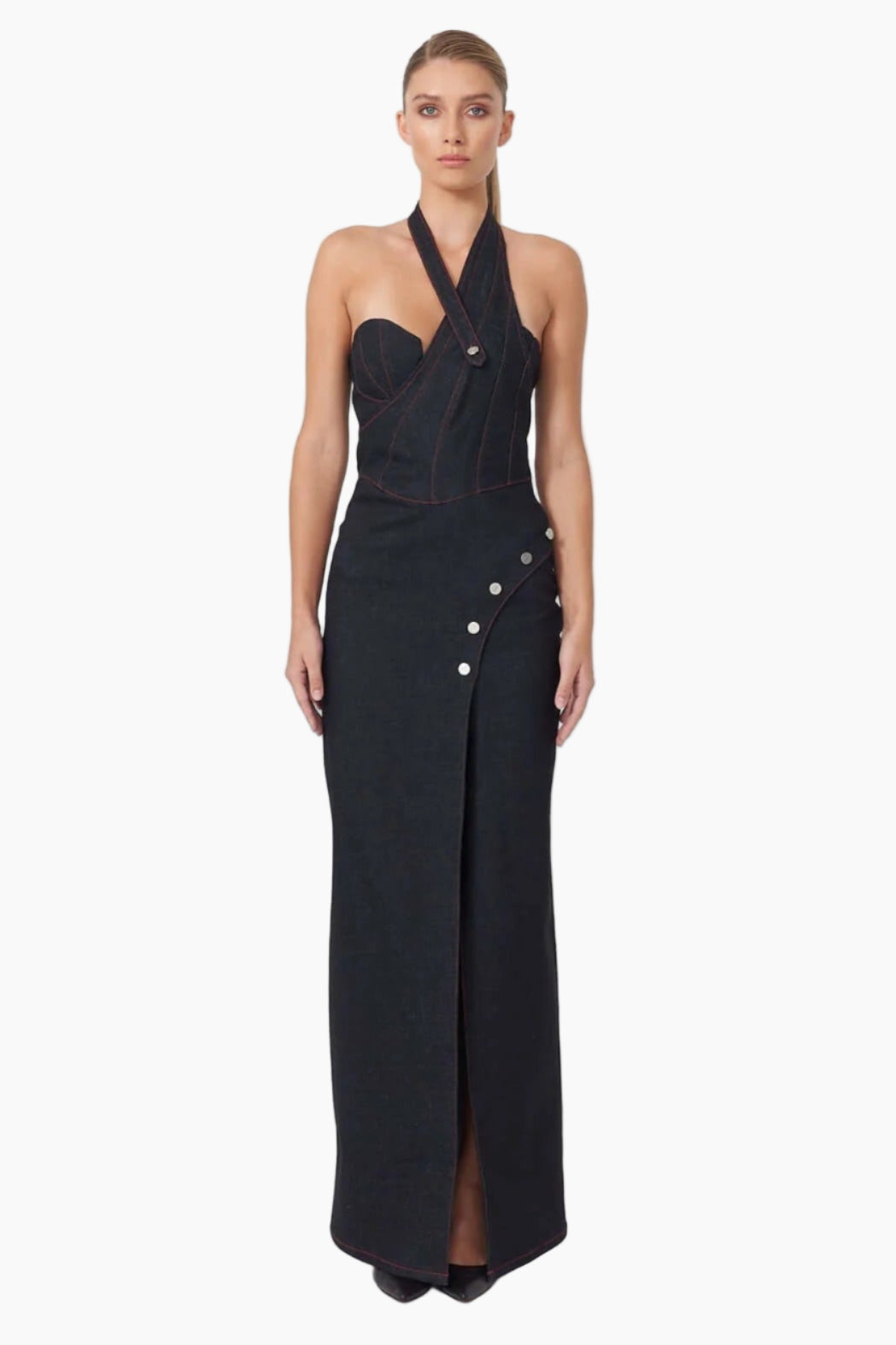 Woman wearing a denim maxi dress. Featuring a clean, asymmetrical design with button details and a thigh-high slit 
