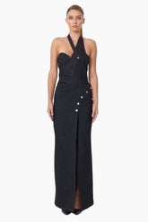 Woman wearing a denim maxi dress. Featuring a clean, asymmetrical design with button details and a thigh-high slit 