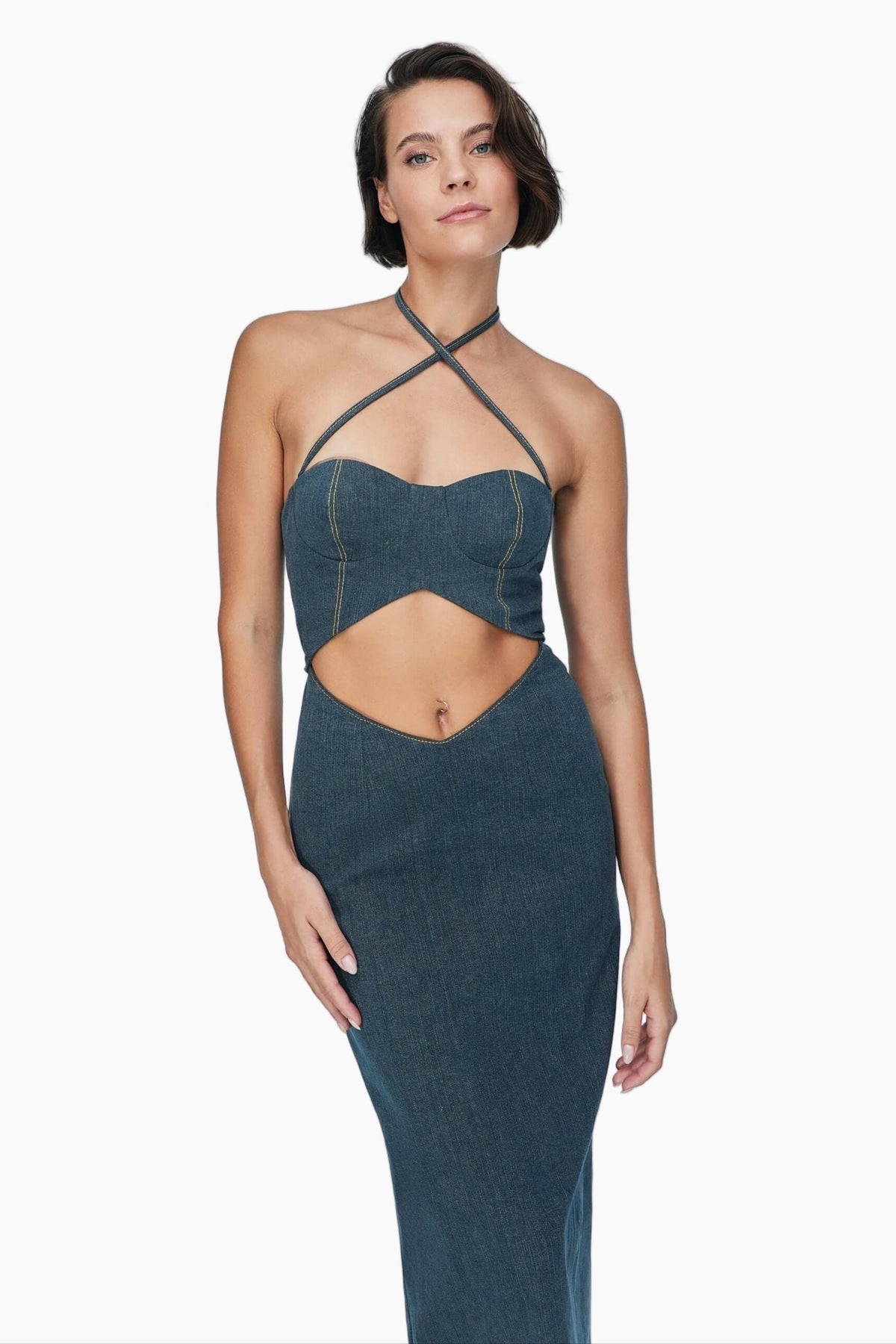 Woman wearing a blue denim maxi dress with delicate cross strap neck, metallic zipper closure and slit detail that extends to the back. 
