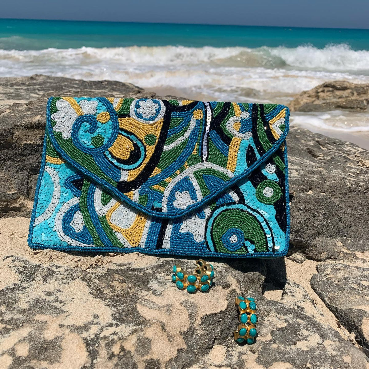 Beaded clutch and earrings on rocks with ocean in the background