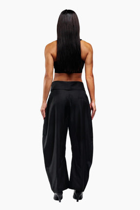 Person wearing a black sleeveless top and wide-leg pants on a white background