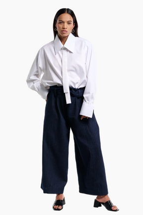 Woman wearing a white blouse and navy wide-leg pants on a white background