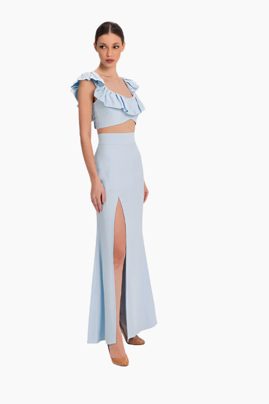 linen set featuring a charming top and skirt ensemble. The top boasts delicate ruffles adorning the neckline. The skirt features a flattering high waist design with a slit in the front.