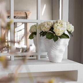 White vase with flowers on a white surface in a bright room