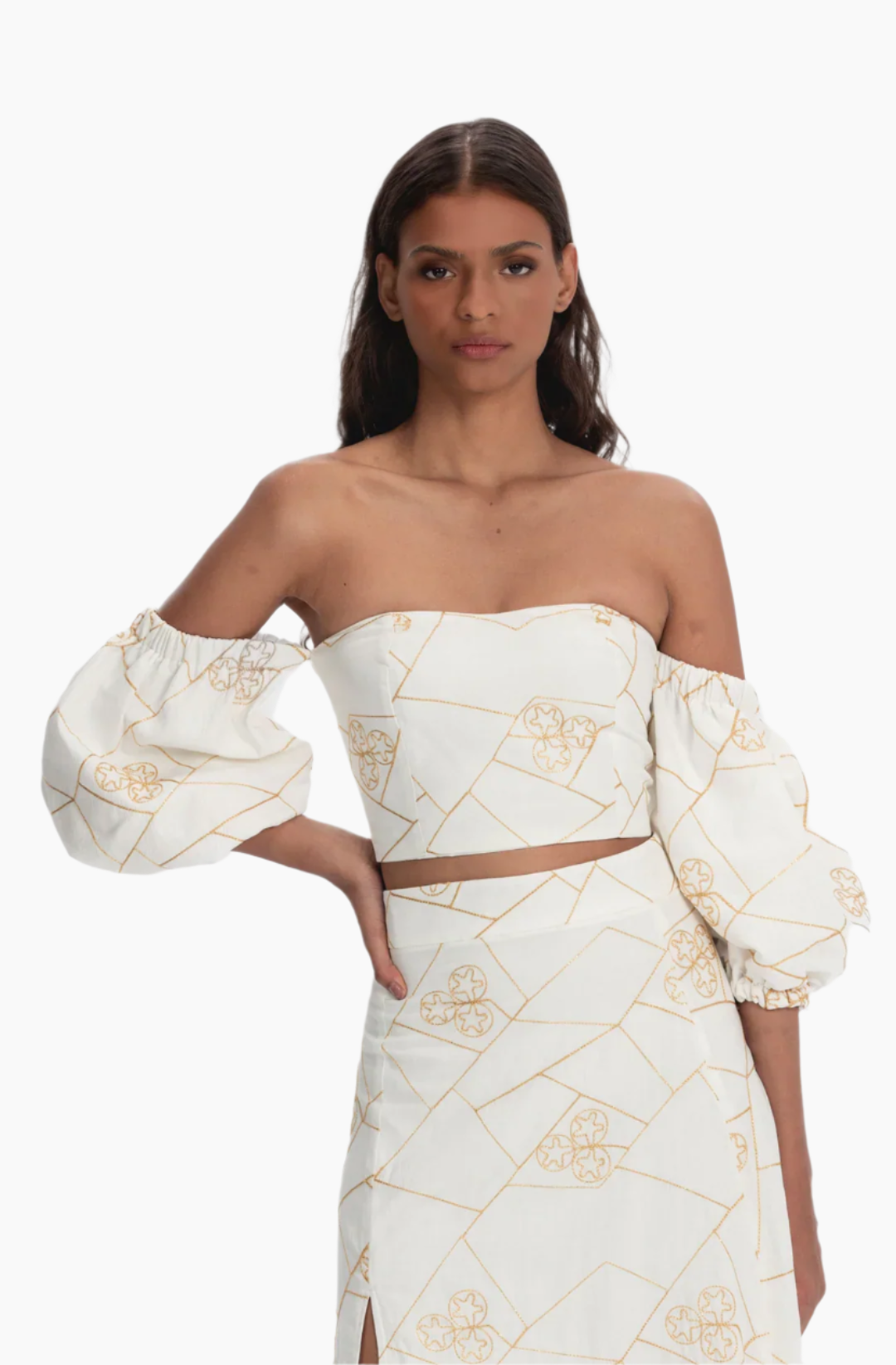 Woman wearing a white and gold patterned outfit. white cotton set,  golden embroidery and voluminous sleeves. slit on the skirt.