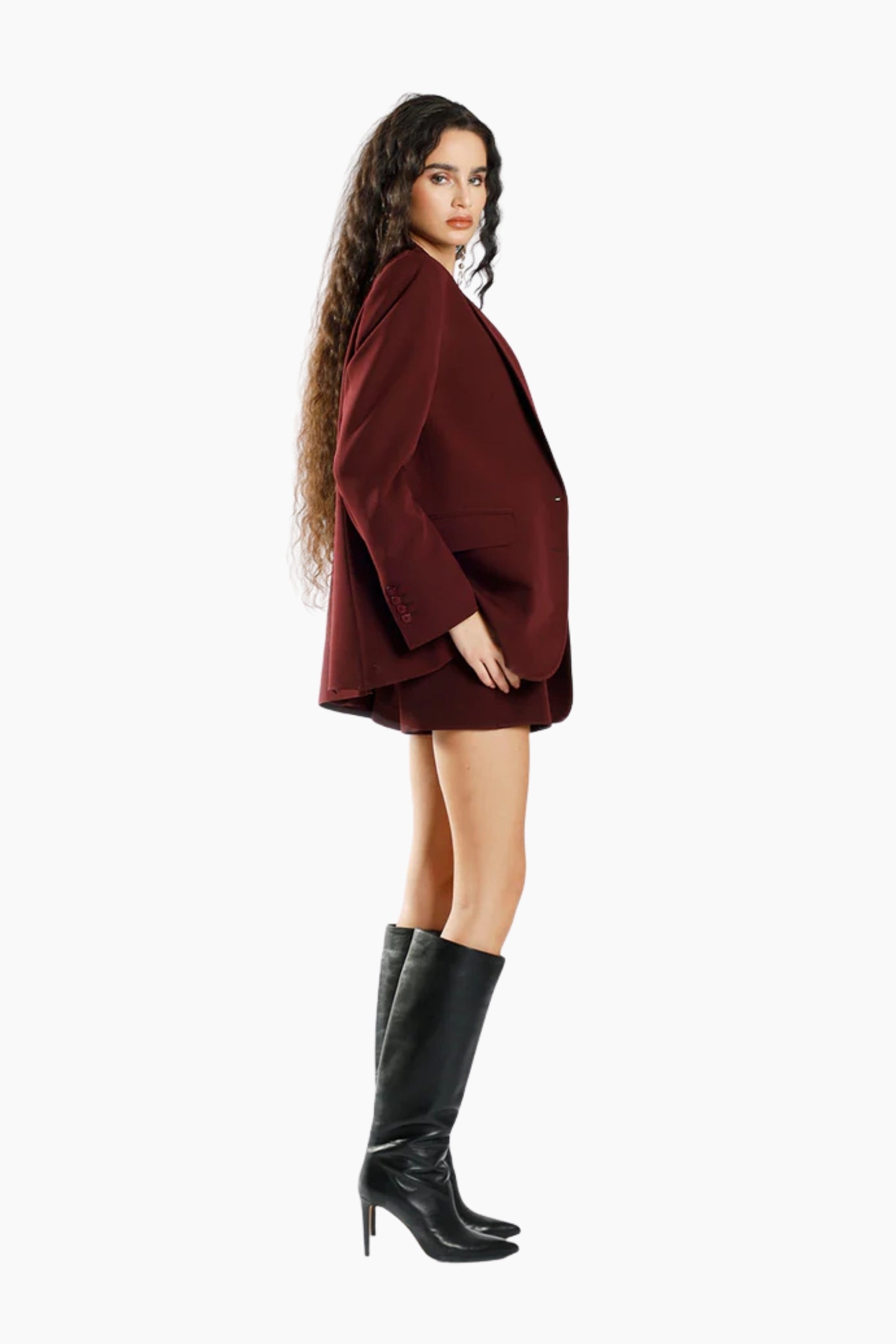 Woman wearing a burgundy coat and black knee-high boots on a white background