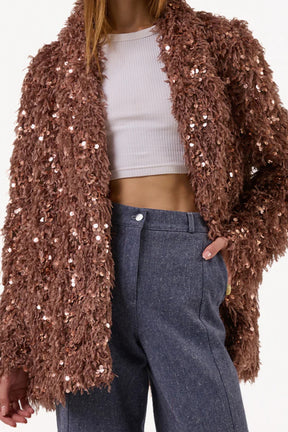 Person wearing a brown sequin cardigan over a white top and blue pants 