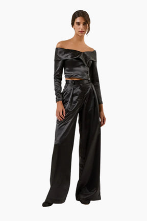Woman wearing a black satin off-shoulder top and wide-leg pants on a white background
