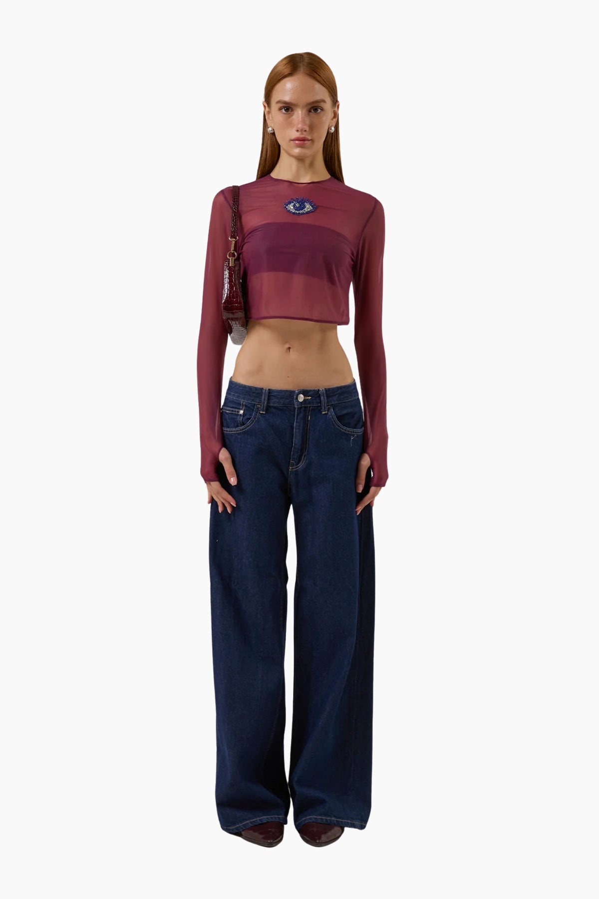 Woman wearing a burgundy long-sleeve crop top and blue jeans on a white background