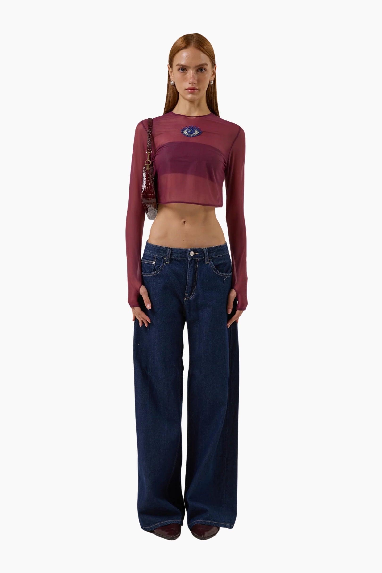 Woman wearing a burgundy long-sleeve crop top and blue jeans on a white background