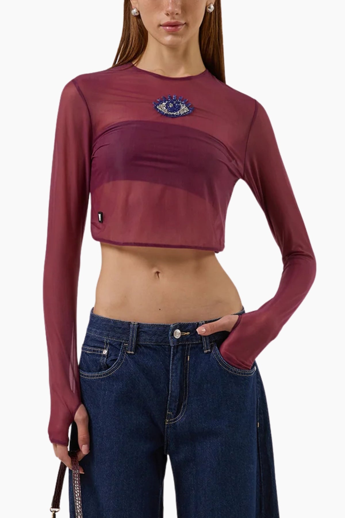Person wearing a burgundy long-sleeve crop top with an eye design and blue jeans on a white background